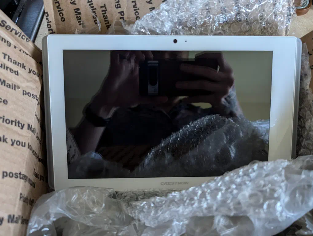 A Crestron tablet sits in a shipping box with bubble wrap in the foreground.