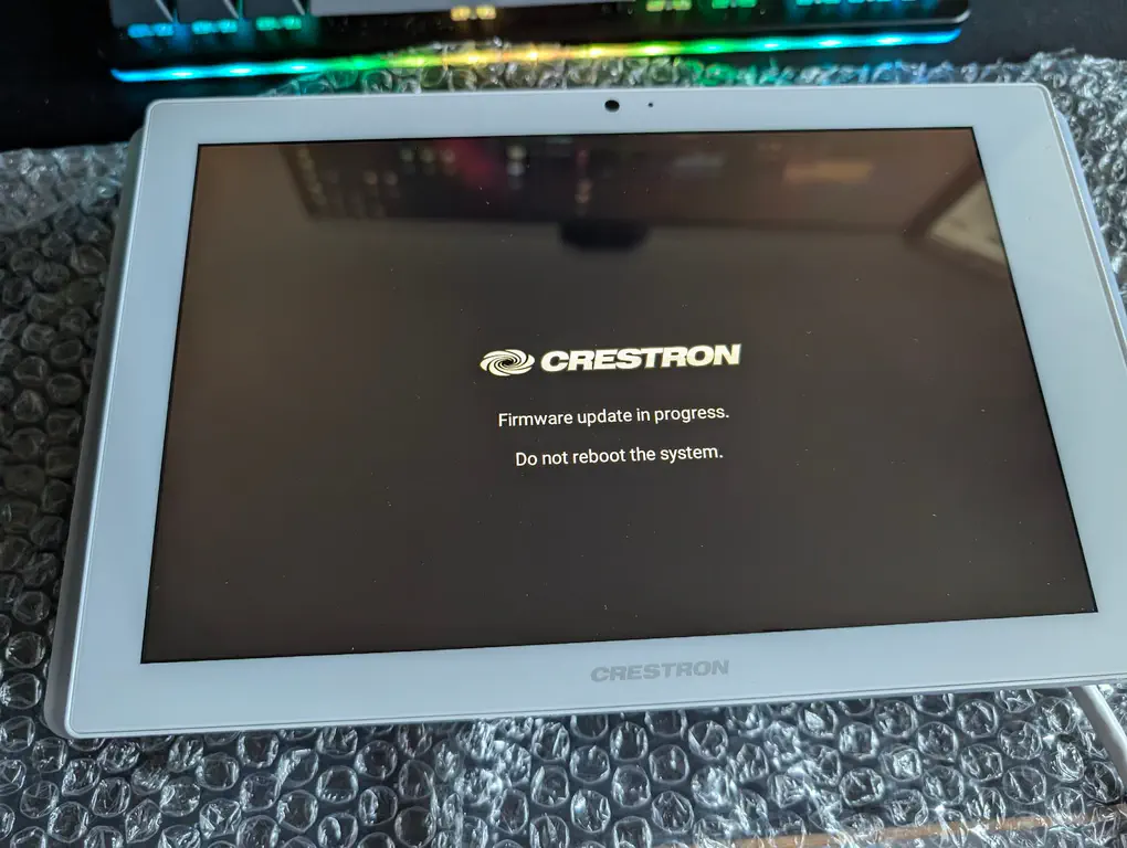 A tablet displays the crestron system firmware update sequence, 'Firmware update in progresse. Do not reboot the system.'
