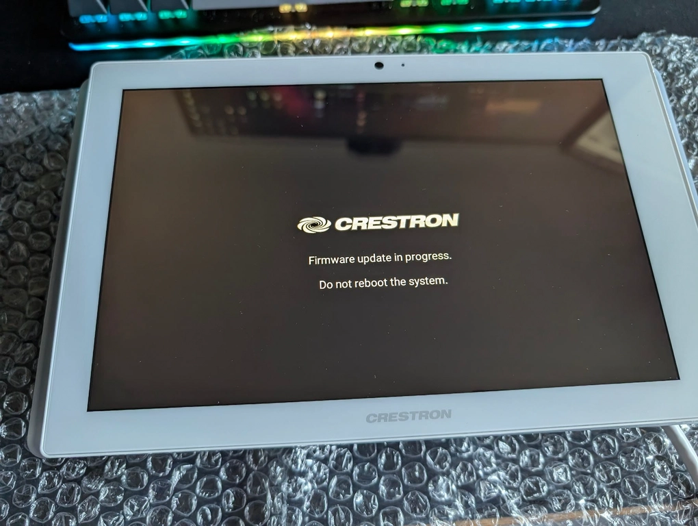 Firmware Upgrade! A tablet displays the crestron system firmware update sequence, 'Firmware update in progresse. Do not reboot the system.'