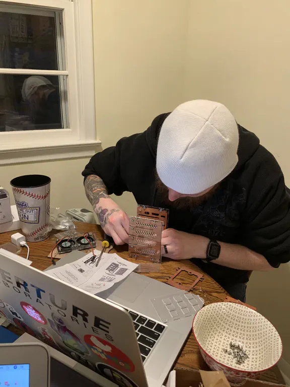 A small kitchen table is full of computers and other wires/gadgets. I'm sitting looking down away from the camera working on the case for what would eventually be a Raspberry Pi Cluster