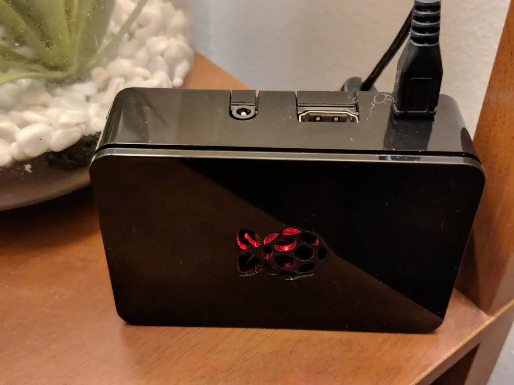 A Raspberry Pi 3 Model B+ is inside of a black glossy enclosure with a red light shining from the center Raspberry cutout.
