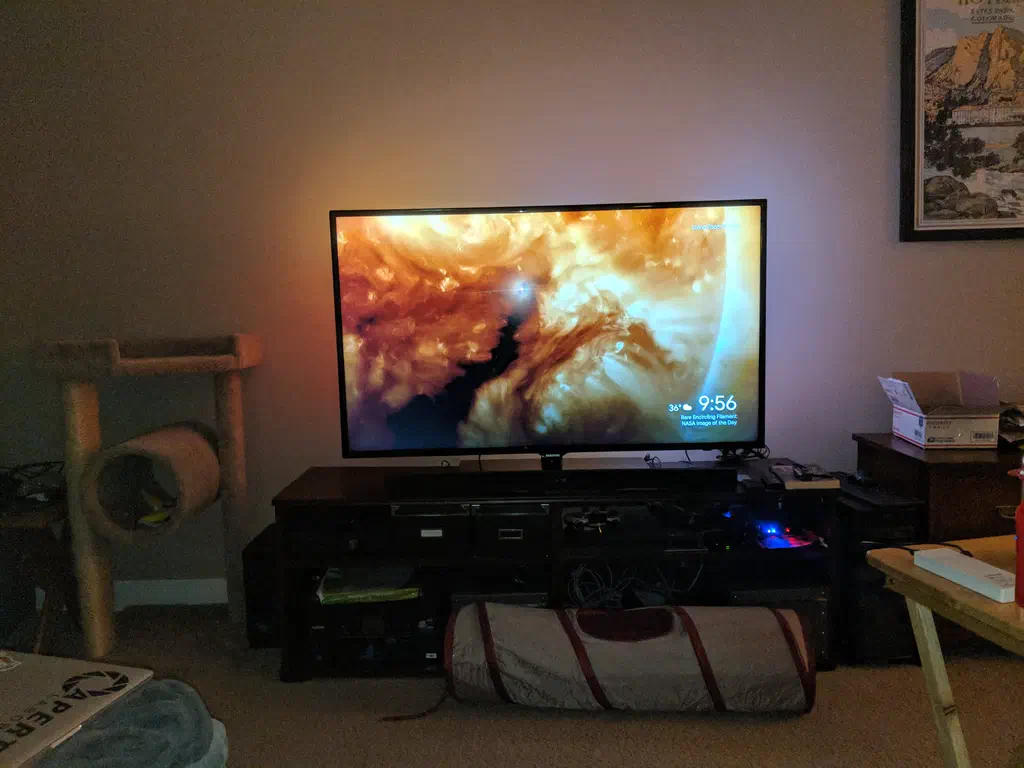 A space scene is on a TV display in a living room. Behind the TV projected on the wall is an ambient glow that maches the scene on the tv.