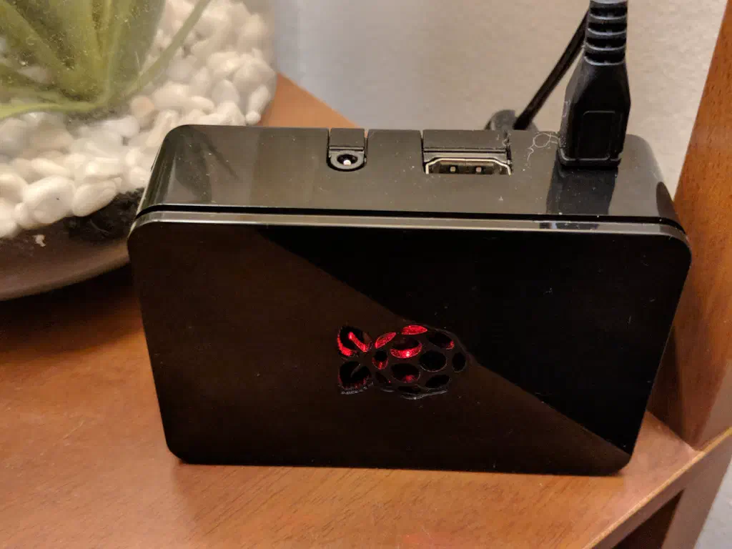A Raspberry Pi 3 Model B+ is inside of a black glossy enclosure with a red light shining from the center Raspberry cutout.